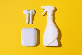 AirPods and case next to unlabeled white plastic spray bottle of household cleaner, against yellow background