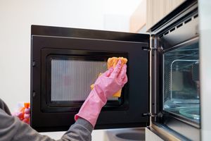 Hands in pink rubber gloves cleaning the door of an open microwave
