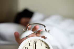What to Know About Daylight Saving Time and Your Health: woman turning off alarm clock