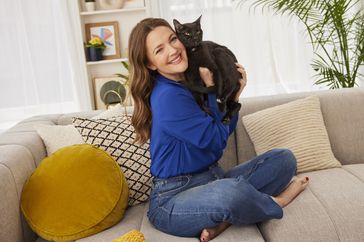 Drew Barrymore sitting on couch holding black cat 