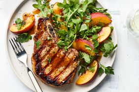 Grilled Pork Chop with Peach-Parsley Salad on a White Circular Plate With Metal Fork