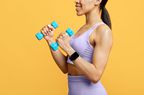 Black woman training with dumbbells and using fitness tracker or smartwatch, yellow background