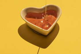 Honey On A Heart Shaped Bowl On Yellow Background