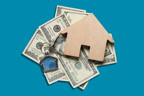 small wooden house decoration, keys with house keychain, and money on blue background
