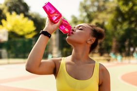 Portrait of sporty black woman in yellow top drinking water