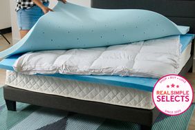 Best Mattress Toppers, tester pulling off the top mattress pad from a stack of matress pads on a bed