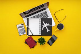 Travel Plan. Personal Organizer, Airplane Model and Passport With Laptop on Yellow Desk.