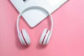 Podcasts to Listen to While Working: headphones and keyboard on a pink background