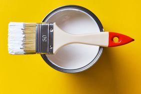 Brush On A Jar Of White Paint, On A Bright Yellow Background. Painting And Repair Work. The concept of creativity, construction work, hobbies.
