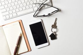 Property agent work desk with house key on a house shaped key chain, computer keyboard, smartphone top view flat lay