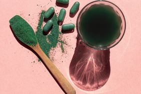 Overhead view of glass with chlorella drink, spirulina and chlorella powder and tablets on a pink background