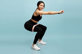 Strength workout concept. woman doing squats with fitness resistance band over blue background