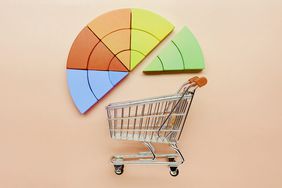 High angle view of pie chart made of colorful building blocks and small shopping cart on pink background