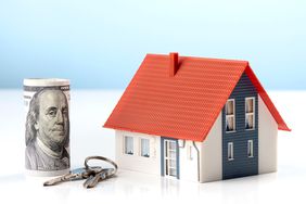 A plastic house, set of keys and money on a white background